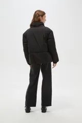 Campera puffer negra con cuello alto, cierre frontal oculto y puños tejidos acanalados. Diseño acolchado con bolsillos laterales.