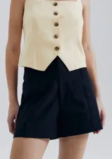 Short de sastre color beige, de tiro alto, con bolsillos laterales tipo ojal y costuras verticales decorativas en el frente.