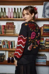 Sweater de lana tejido a mano color negro con bordado de flores rosas, naranjas y rojas. Tiene cuello redondo y mangas largas con puños ajustados.