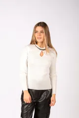 Sweater de punto acanalado color blanco, con mangas largas y detalle de abertura tipo gota en el escote, decorado con una cadena metálica oscura en el cuello.
