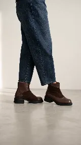 Bota corta de cuero color marrón, con diseño de texturas combinadas, talón con textura grabada, taco geométrico y cierre lateral.