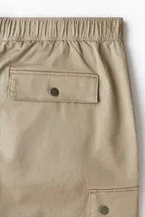 Pantalón cargo de algodón color beige, con corte holgado y diseño amplio. Cuenta con bolsillos laterales de fuelle y pliegues en las rodillas.