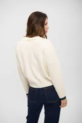 Buzo de tejido de punto color crema con cuello polo y detalles en color verde oscuro en el cuello y los puños. Presenta un diseño de manga larga con textura acanalada en los antebrazos y corte recto.