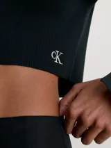 Cárdigan negro de punto acanalado elástico, corte slim cropped, manga larga con abertura en el puño y cierre frontal con corchetes. Presenta el logo 'ck' bordado en blanco en el bajo.