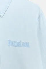 Camisa de denim en tono celeste claro, de manga larga con puños abotonados, cuello camisero clásico y cierre frontal de botones. Cuenta con el logotipo de Fruit of the Loom bordado a tono en el pecho.