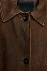 Abrigo largo de piel con cuello solapa, manga larga y cierre frontal con botones. Presenta bolsillos delanteros y forro interior.