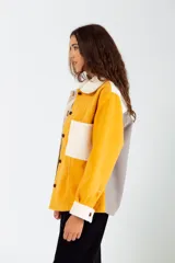 Camisa de paño color mostaza, con cuello camisero, cierre frontal con botones marrones, manga larga con puños abotonados, bolsillo de parche en el pecho y corte oversize.