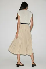 Vestido midi bicolor con parte superior blanca de escote en V cruzado con ribete negro y falda plisada en color tostado. Cuenta con mangas sisa, cintura elástica y un cinturón negro tipo reptil con hebilla ovalada.