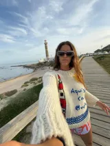 Sweater de lana color crema, tejido y bordado a mano con motivos de faro, sol y la frase "Aquí solo corre el viento".