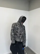 Buzo con cierre frontal completo, confeccionado en tejido de punto grueso de algodón. Presenta un diseño estampado integral con motivos gráficos y tipografía estilo gótico en tonos gris y negro, capucha integrada, puños y ruedo acanalados en color negro sólido.