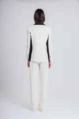 Blazer de corte sastrero en color marfil con detalles en negro en solapas, laterales y bolsillos. Presenta cierre frontal con dos botones y diseño estructurado.