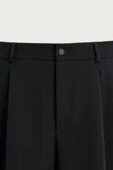 Pantalón relaxed fit marrón oscuro, de corte ancho y recto, con pliegues frontales, bolsillos laterales y cierre con botón y cremallera.