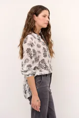 Camisa blanca de manga larga con estampado botánico en tono oscuro, cuello mao y escote en V con cierre frontal parcial de botones.
