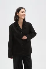 Chaqueta de gamuza sintética en color negro, con cuello solapa, cierre frontal con botones y bolsillos delanteros. Presenta un corte holgado y mangas largas.