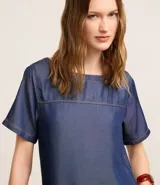 Vestido corto de color azul claro, confeccionado en liocel, con cuello redondo, mangas cortas y detalle de costura horizontal en el busto. Cuenta con bolsillos laterales.