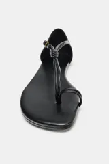 Sandalia plana de cuero negro con diseño de dedo, detalle de nudo en la tira central y cierre con hebilla metálica lateral.