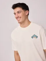 Remera holgada de algodón color beige, de manga corta y cuello redondo, con un gran estampado colorido en la espalda con diseño de olas y la inscripción 'Rusty Tribe'.