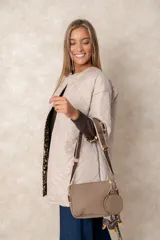 Cartera bandolera color chocolate con textura granulada, que incluye un monedero circular desmontable sujeto a la correa. Posee cierre superior y correa ajustable con detalles en color crema.