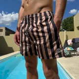 Short de baño con diseño de rayas verticales en color verde menta y negro. Cuenta con cintura elástica con cordón ajustable y un parche circular con logo en la parte inferior.