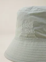Gorro tipo bucket color celeste con logo bordado "Benson & Thomas Modern Classics" en el frente.