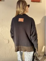 Buzo de tejido de punto grueso en color verde oliva con diseño jacquard en tonos grises y blancos. Presenta cuello redondo, mangas largas y terminaciones acanaladas en puños y ruedo.