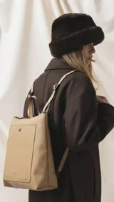 Mochila de diseño moderno y funcional, confeccionada en símil cuero con textura granulada. Cuenta con un bolsillo frontal con broche, cierre principal superior, manija superior y correas ajustables. Incluye logo de la marca grabado en el frente.