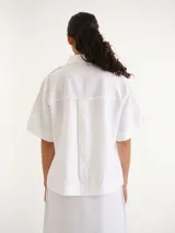 Camisa de manga corta blanca, con cuello camisero, cierre frontal de botones y diseño recto.