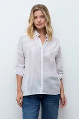 Camisa de corte holgado con diseño de rayas verticales en tonos beige y blanco, con sutiles destellos brillantes. Presenta cuello clásico, cierre frontal con botones y mangas largas con puños ajustables.