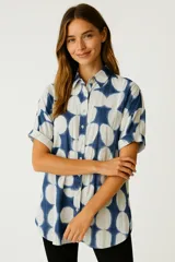 Camisa de corte holgado con estampado de círculos grandes en tonos azul y blanco. Presenta cuello camisero clásico, cierre frontal con botones y mangas cortas con dobladillo.