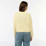 Cardigan de punto color amarillo suave, con cuello redondo, cierre frontal de botones y dos bolsillos de parche delanteros. Presenta mangas largas con puños acanalados y un corte recto.