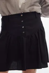 Falda corta de algodón color negro, con volados, cartera de botones frontal y diseño de tiro alto con corte curvo en la cintura.