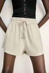 Bermuda color crema confeccionada en lino, de tiro alto con cintura elástica ajustable con cordones y bolsillos delanteros.