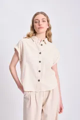 Camisa casual de lino color crudo, con cuello camisero, manga corta doblada y cierre frontal con botones oscuros.