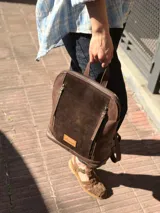 Mochila color chocolate combinada en cuero y gamuza, con cierre principal y bolsillos frontales con cierres verticales. Cuenta con asa superior y correas ajustables.