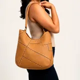 Cartera al hombro Korium modelo Aster, de diseño slouchy en color tostado, decorada con costuras geométricas y tachas metálicas doradas y plateadas. Cuenta con asa fija para llevar al hombro.