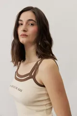 Musculosa de tejido rib color beige con detalles en marrón oscuro en el escote y doble tirante fino. Presenta un pequeño texto estampado en el pecho.