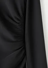 Vestido midi negro de manga larga, con cuello alto drapeado y corte estructurado en la cintura, falda acampanada de caída suave.