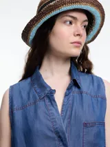 Camisa sin mangas en denim 100% lyocell, muy liviano con caída fluida. De corte recto y largo medio, presenta cartera escondida en el frente y un bolsillo plaqué en el pecho. En la espalda, un detalle distintivo: botones decorativos alineados en abertura vertical. Los pespuntes a contratono completan el look.