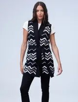 Chaleco largo tejido con cuello solapa, bolsillos delanteros, pasadores en la cintura y lazo para ajustar. Diseño con patrón de zigzag en blanco y negro.