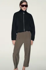 Pantalón de tiro medio con pinzas delanteras, bolsillos laterales y falsos bolsillos de vivo en la parte trasera. Presenta un corte holgado que se estrecha hacia el tobillo, con bajo acabado en pliegues y cierre frontal con cremallera, botón interior y gancho.