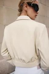 Camisa crop de manga larga con cuello solapa y cierre frontal de botones, confeccionada en tejido sintético con efecto piel color beige.