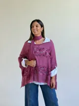 Sweater de punto magenta con diseño holgado, cuello redondo y detalles de encaje floral aplicado en el frente. Incluye una bufanda tipo choker integrada del mismo tejido.