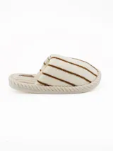 Pantuflas abiertas de estilo mule, con capellada de peluche color crema con rayas negras horizontales y plantilla de pana acanalada en tono beige.