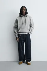 Sudadera tipo hoodie de corte relajado, confeccionada en tejido de algodón con interior cepillado. Presenta capucha con cordones ajustables, bolsillo frontal tipo canguro y terminaciones en rib en puños y ruedo.