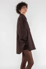 Camisa acolchada marrón con cuello clásico, cierre frontal con botones, manga larga raglán, puños abotonados, bolsillo utilitario en el pecho, bolsillos laterales y canesú abotonado en la espalda.