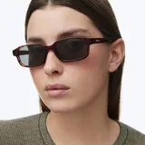 Lentes de sol modelo Kya de silueta rectangular oversized, con montura gruesa de carey y lentes polarizadas oscuras.