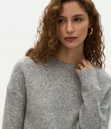 Suéter de punto jaspeado en color gris oscuro, con cuello redondo y mangas largas. Presenta un diseño integrado con una camisa blanca debajo, creando un efecto de capas superpuestas.