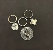 Set de tres llaveros de metal plateado con motivos religiosos, incluyendo un dije circular con la imagen del Sagrado Corazón de Jesús, un dije circular pequeño con una cruz y un dije con forma de cruz griega.