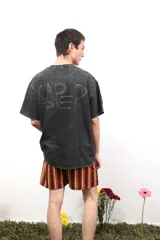 Remera de algodón con efecto lavado ácido en color negro, de corte holgado y manga corta. Presenta un estampado artístico en color rojo en la parte posterior con la palabra Caper.
