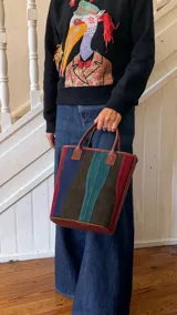 Matera de cuero con diseño de paneles verticales en combinación de colores azul, verde, marrón y bordó. Cuenta con dos asas cortas de cuero y estructura rígida.